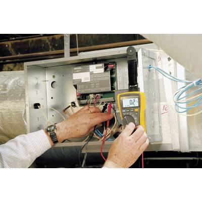 Eine Person misst die Elektrik eines Lüftungssystems mit einem gelben Multimeter, das '0.2' anzeigt, und prüft Kabelverbindungen.