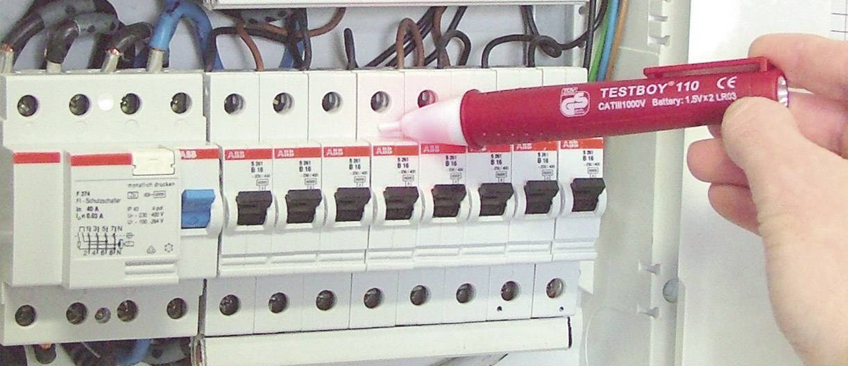 Person testet mit Spannungsprüfer die Sicherungen in einem geöffneten Sicherungskasten. Der Prüfer leuchtet auf einer Sicherung.