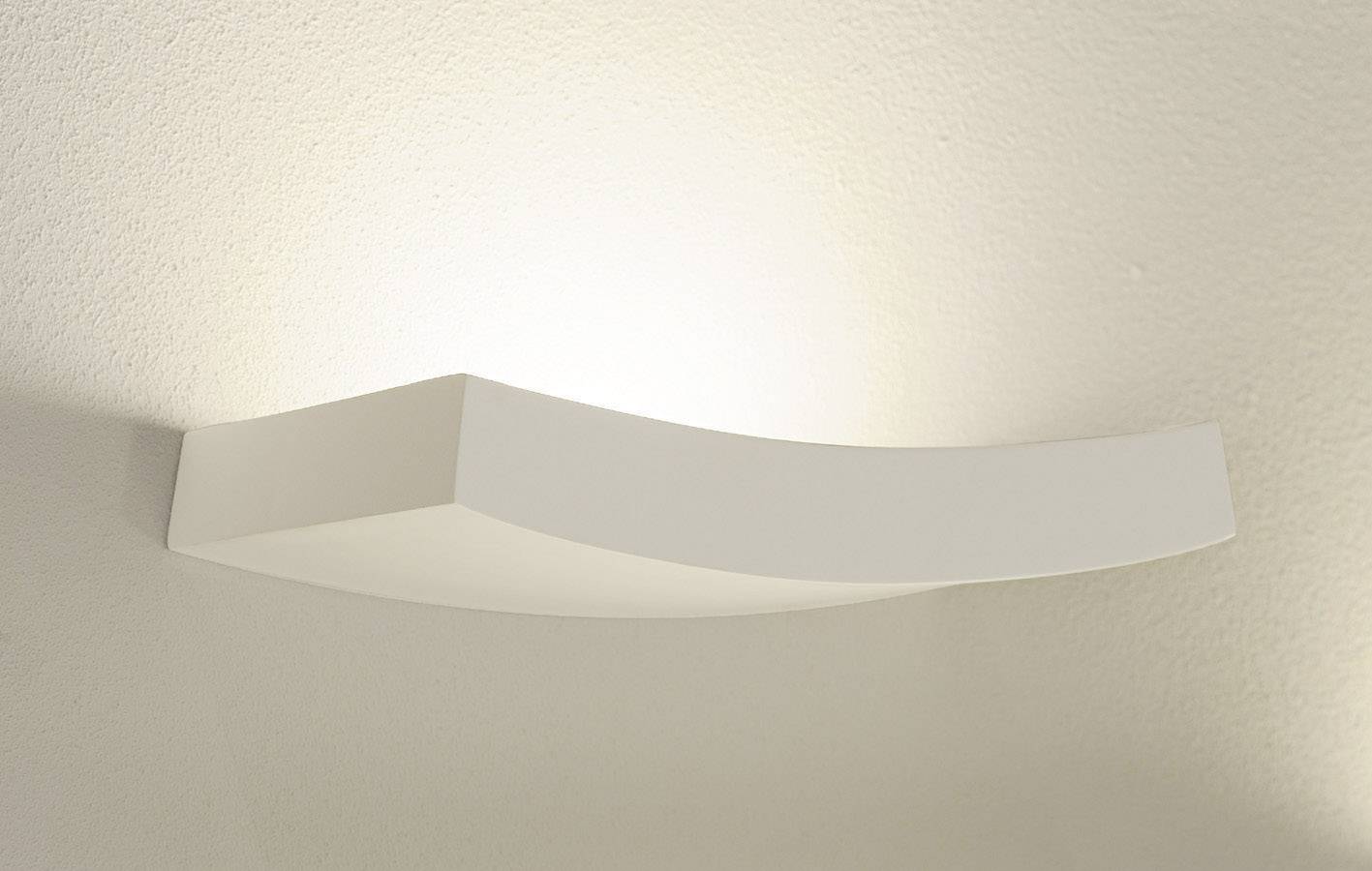 Wandleuchte in geschwungener Form montiert an einer weißen Wand. Diffuses Licht strahlt nach oben und erzeugt eine warme Atmosphäre.