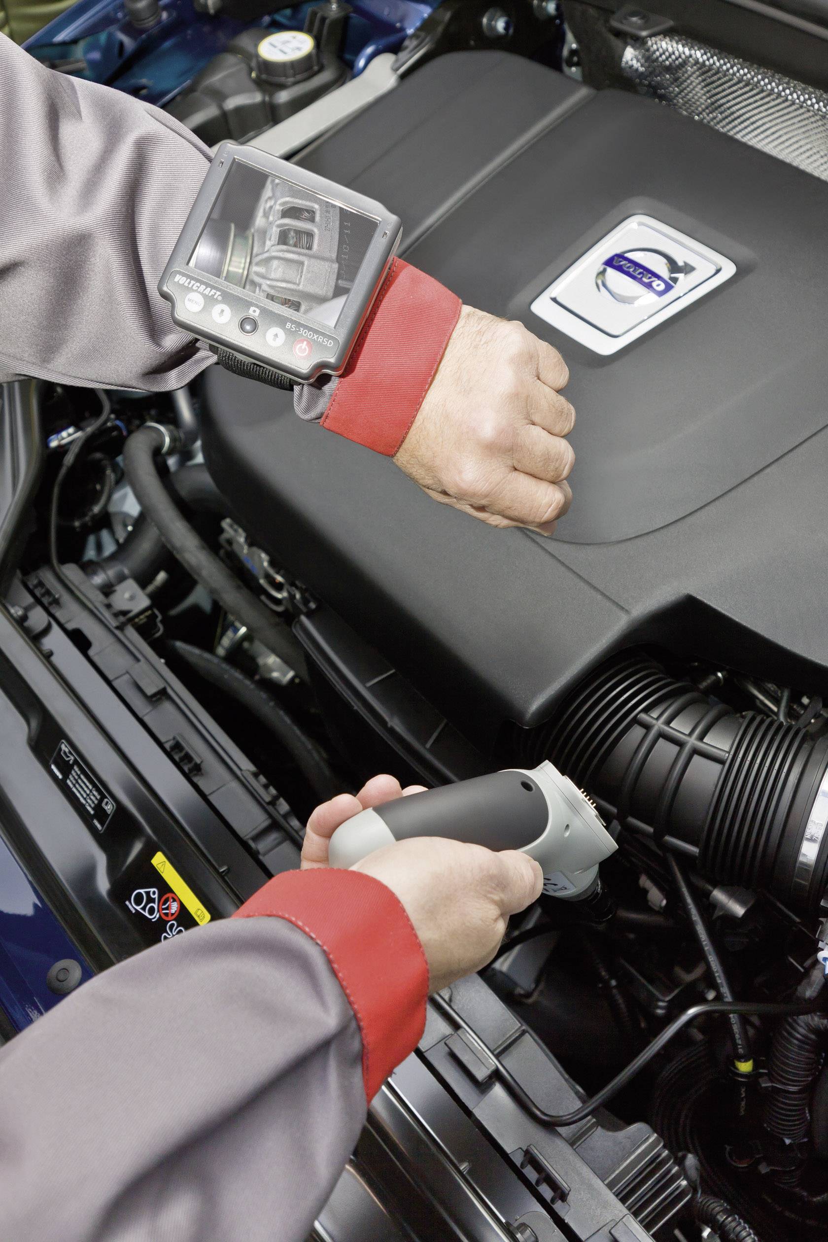 Ein Mechaniker überprüft einen Automotor mit einem Handgerät. Ein Bildschirm am Handgelenk zeigt Details des Motors.