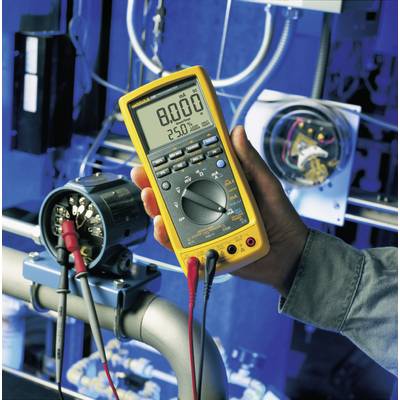 Eine Hand hält ein gelbes Multimeter, das elektrische Spannung an einem technischen Gerät misst, auf dem Display steht '8.000'.