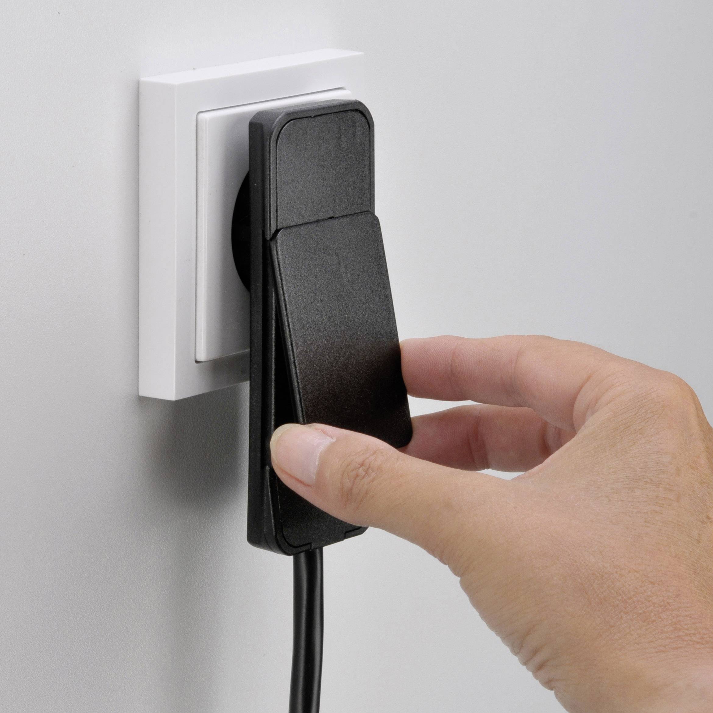 Eine Hand steckt einen schwarzen Stecker in eine weiße Steckdose an der Wand.