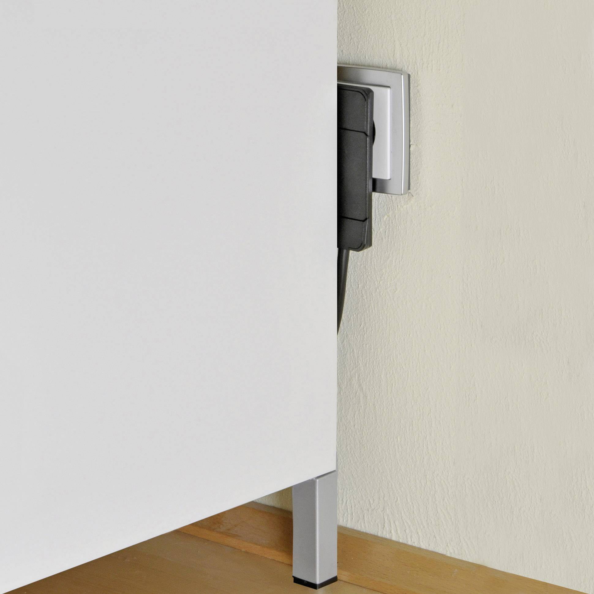Ein weißer Schrank steht neben einer Wandsteckdose, in die ein schwarzes Kabel eingesteckt ist.