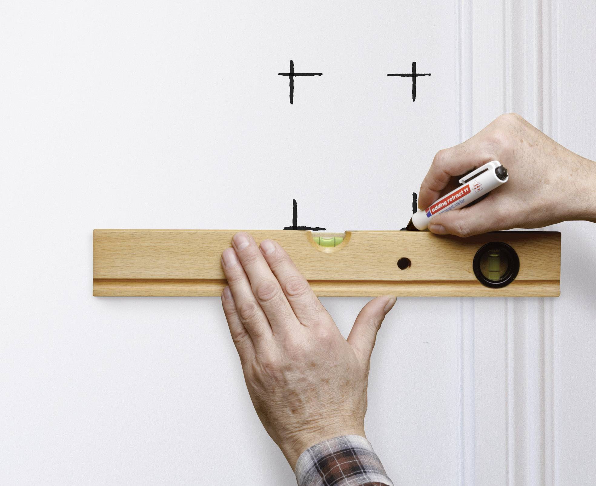 Eine Person markiert mit einer Wasserwaage und einem Stift zwei Bohrlöcher an einer weißen Wand.