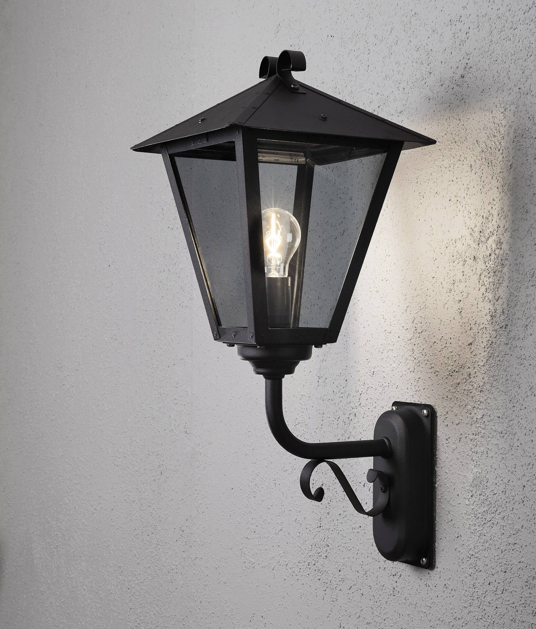 Schwarze Wandlaterne mit freiliegender Glühbirne an einer grauen Wand montiert, leuchtet im Innen- oder Außenbereich.