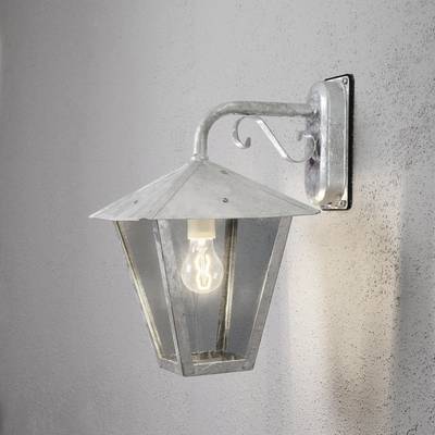 Eine silberne, sechseckige Wandleuchte mit Glühbirne an einer grauen Wand montiert. Die Lampe hat ein schlichtes, antikes Design.