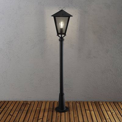 Schwarze, klassische Laterne leuchtet auf hölzernem Boden vor grauer Wand, Beleuchtung sorgt für warme Atmosphäre.