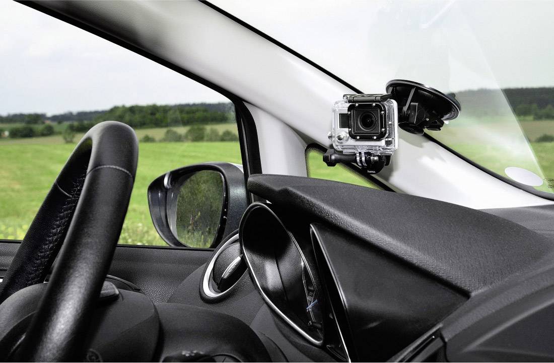 Eine Action-Kamera ist im Inneren eines Autos an der Windschutzscheibe angebracht, mit grüner Landschaft im Hintergrund.