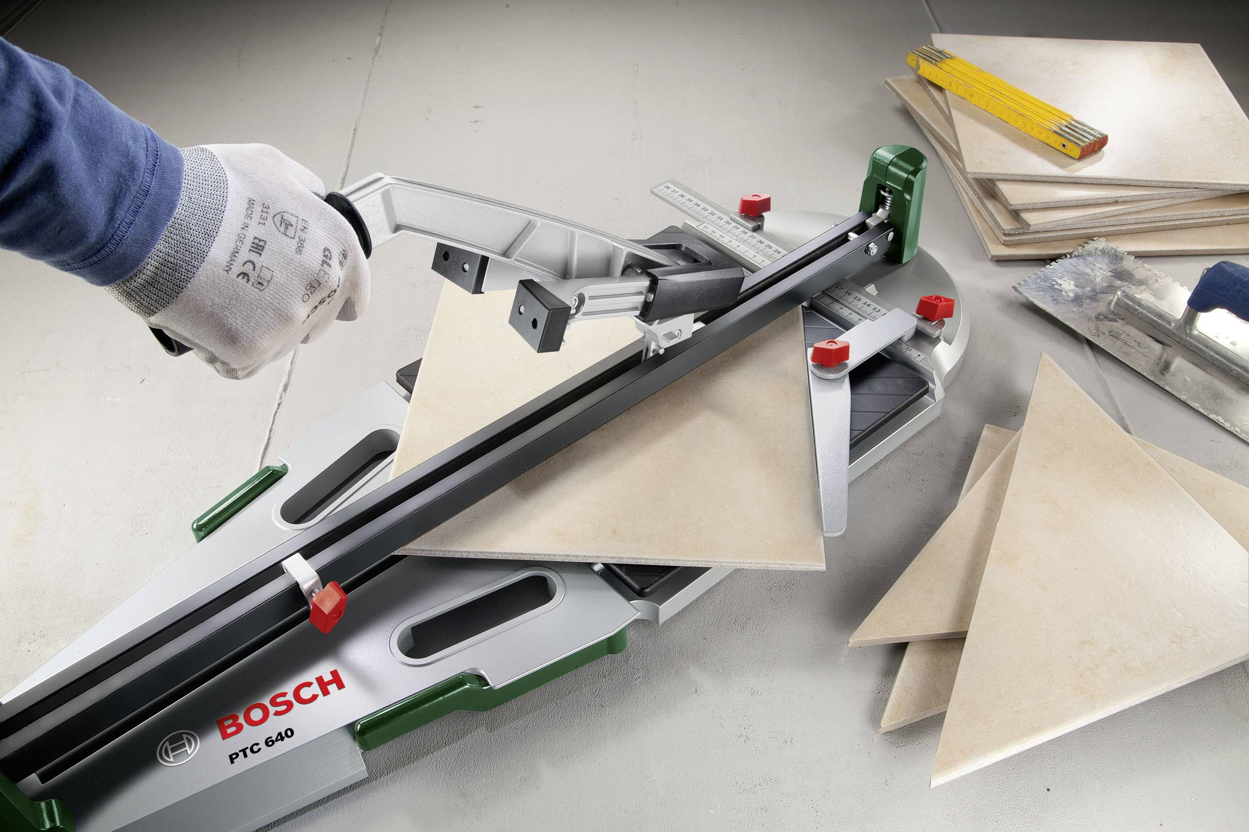 Ein Fliesenschneider von Bosch, das Modell PTC 640, schneidet eine quadratische Fliese in Dreiecke. Links eine Hand in einem Handschuh.