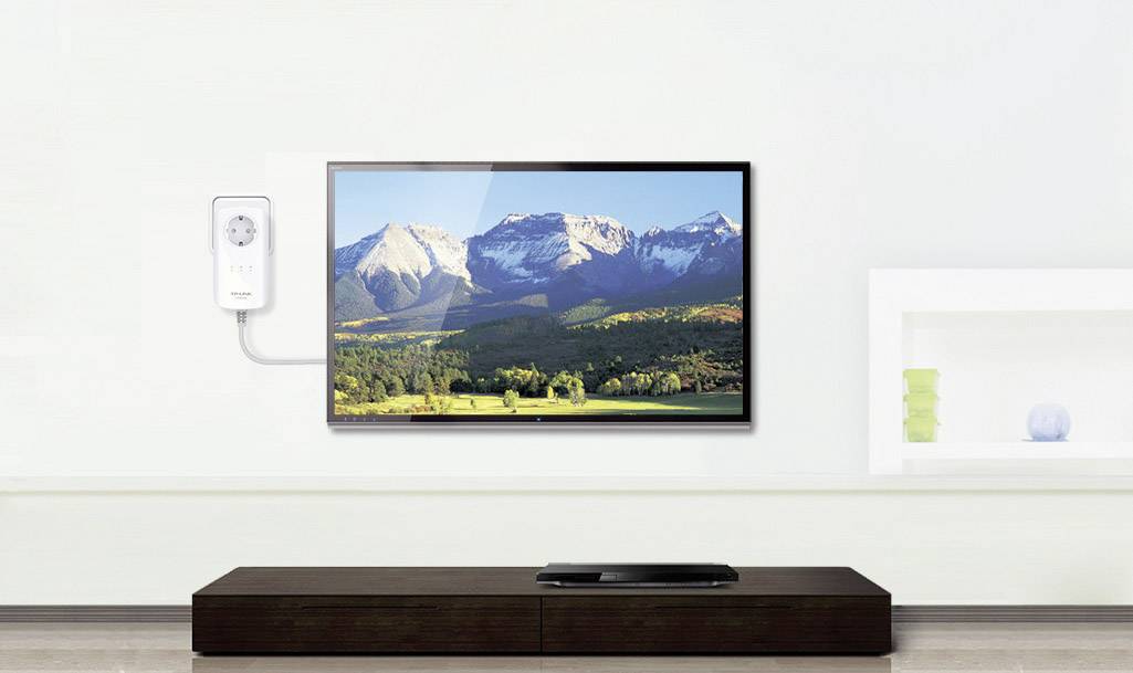 Flachbildfernseher an weißer Wand zeigt Landschaft mit Bergen und Wäldern. Darunter ein braunes Lowboard, leer bis auf ein Gerät.