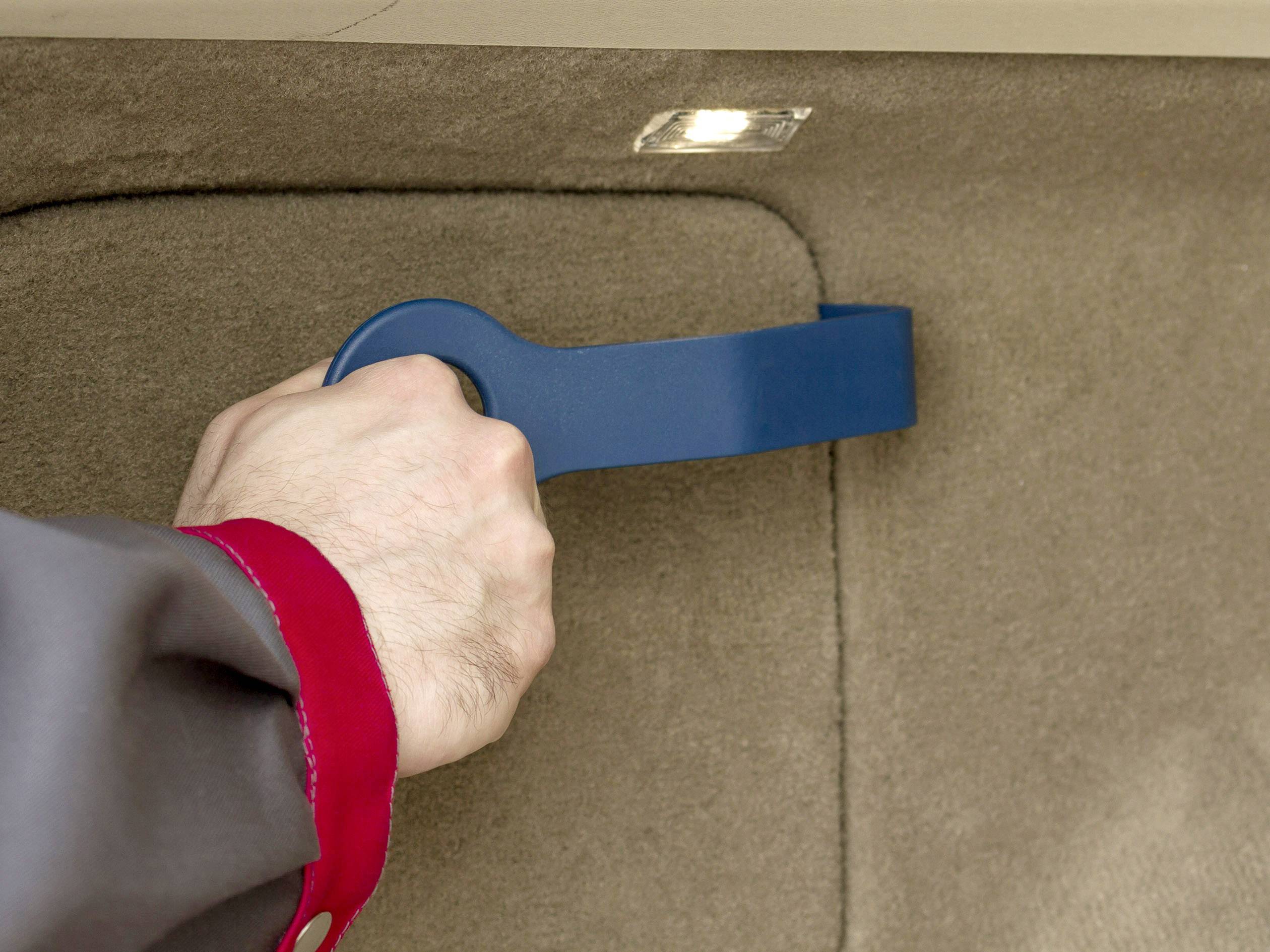 Eine Person zieht an einem blauen Hebel im Inneren eines Autos. Der Hebel ist möglicherweise Teil der Kofferraumentriegelung.