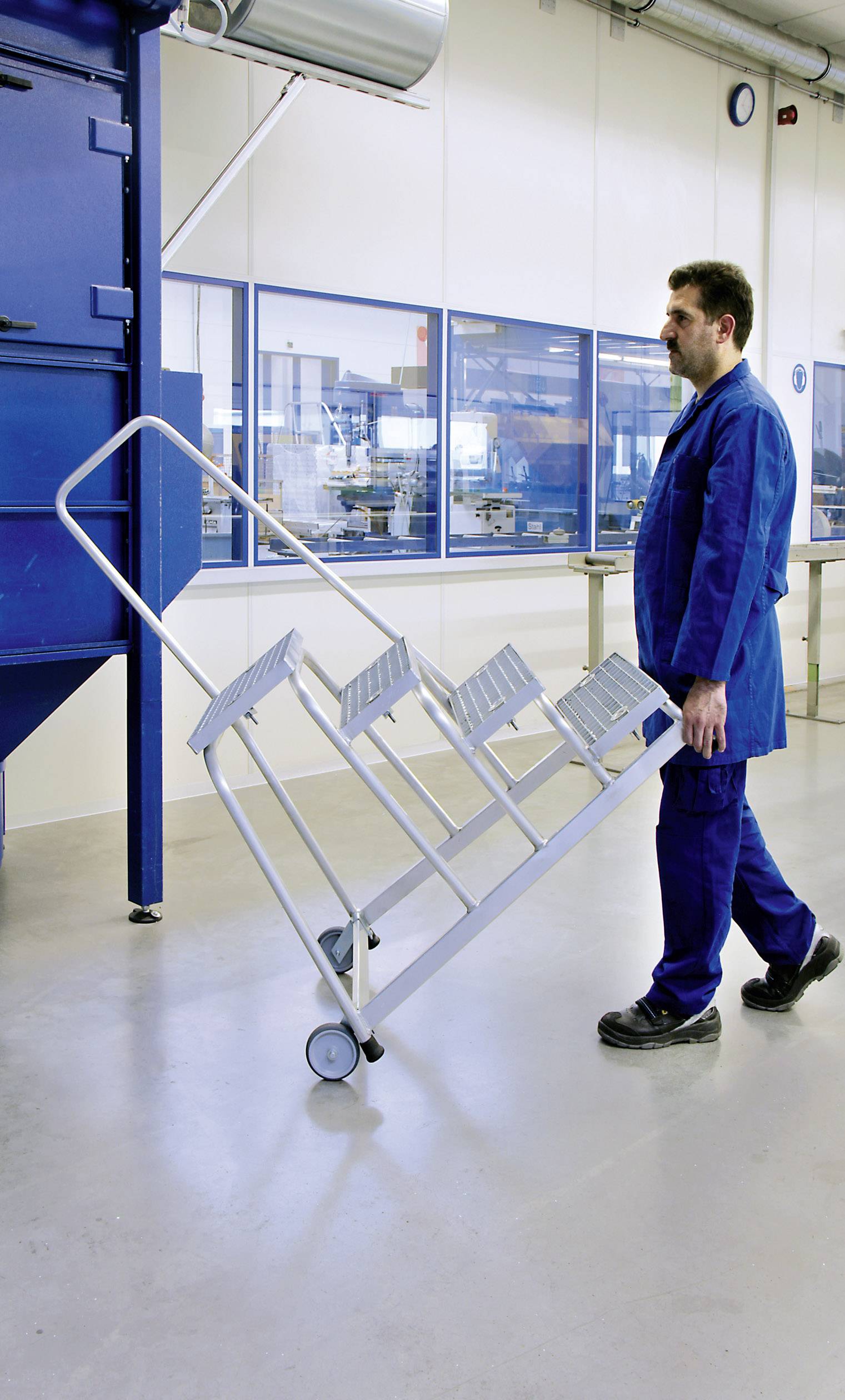 Ein Mann in Arbeitskleidung kippt einen handbetriebenen Transportwagen in einer industriellen Umgebung.