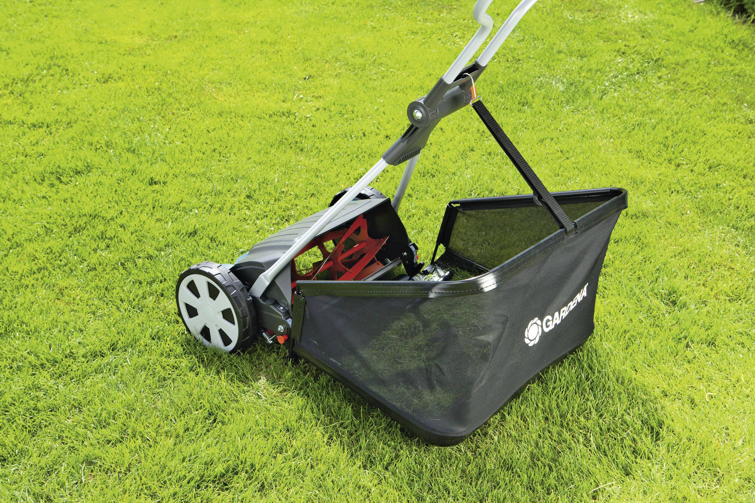 Ein Handrasenmäher mit Auffangkorb auf grünem Rasen. Der Mäher hat Räder und einen ergonomischen Griff.