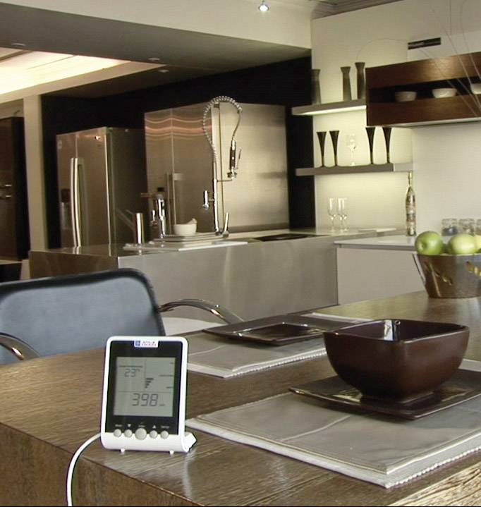 Moderne Küche mit Edelstahlgeräten, zentrale Kochinsel und Essbereich. Im Vordergrund ein digitales Thermometer mit Anzeige.