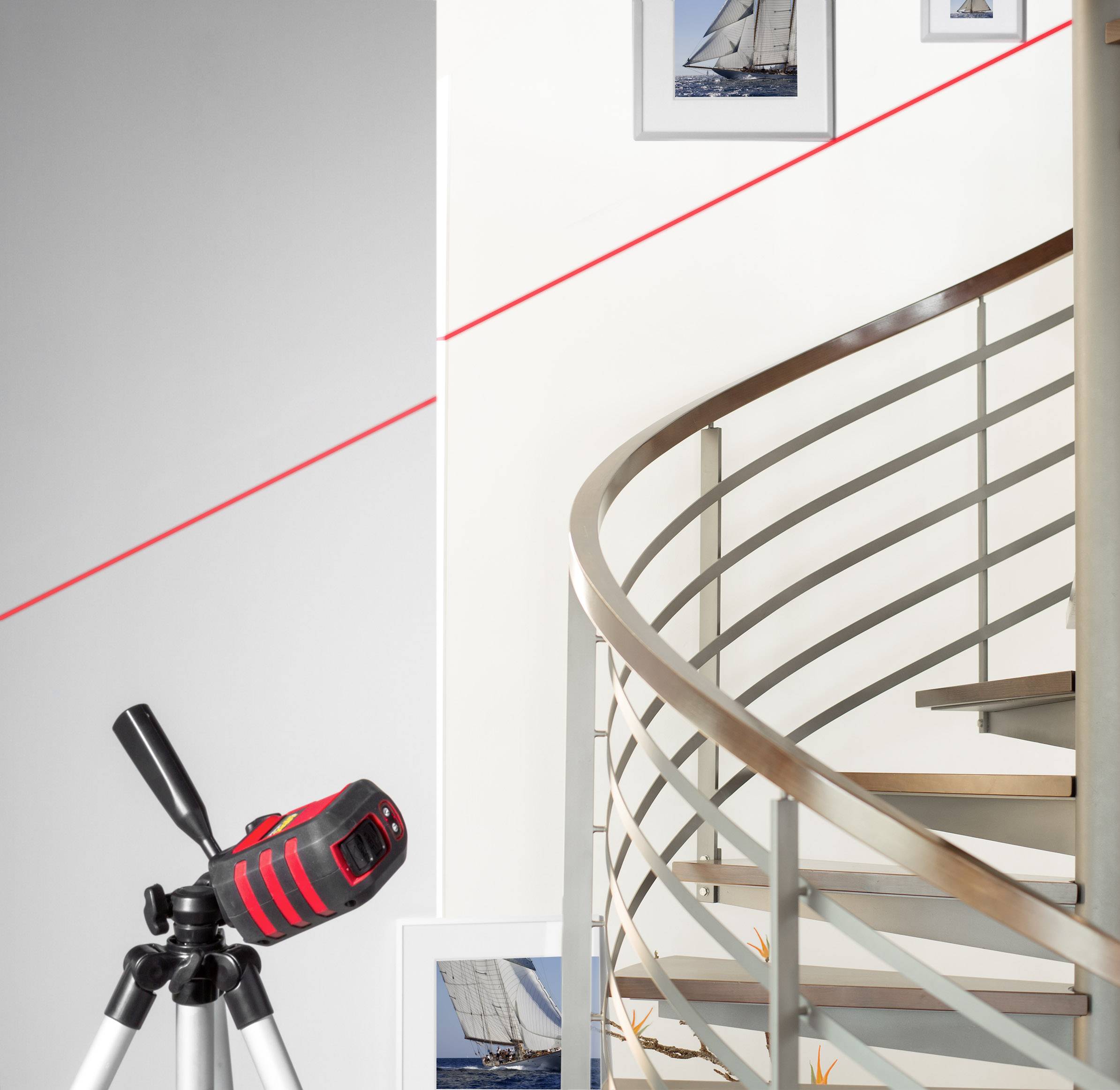 Ein modernes Interieur zeigt ein Metallwendeltreppe, ein Stativ mit einem roten Gerät und Bilder von Segelbooten an der Wand.