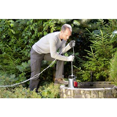 Eine Person sammelt Wasser aus einem Brunnen mit Hilfe einer Tauchpumpe in einem bewaldeten Gartenbereich.
