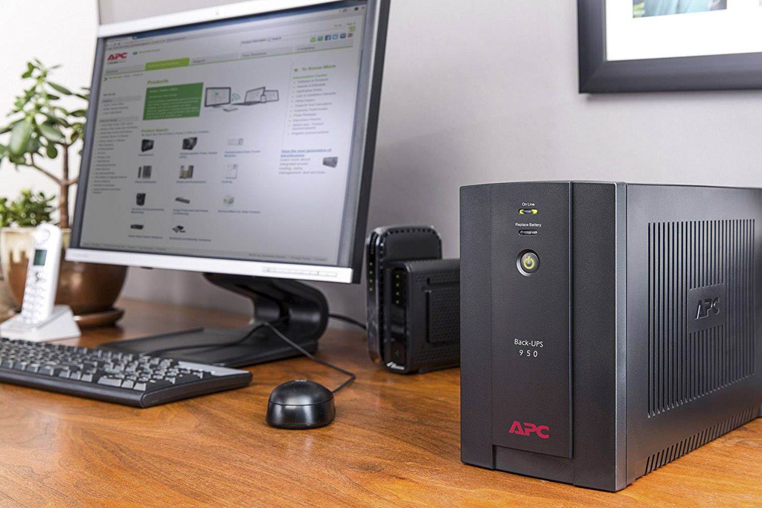Ein Desktop-Computer mit einem Monitor zeigt eine Webseite an. Daneben steht eine APC-Black-UPS-950-Einheit auf einem Holztisch.