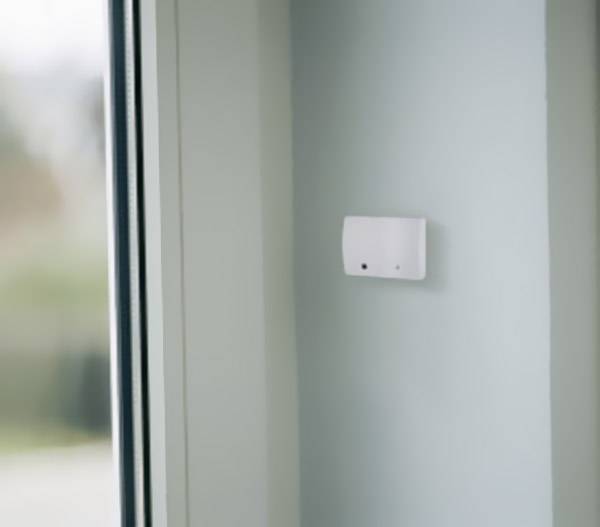 Ein Wandthermostat an einer blassgrünen Wand neben einem Fenster, das Teil eines Heizungssteuerungssystems sein könnte.