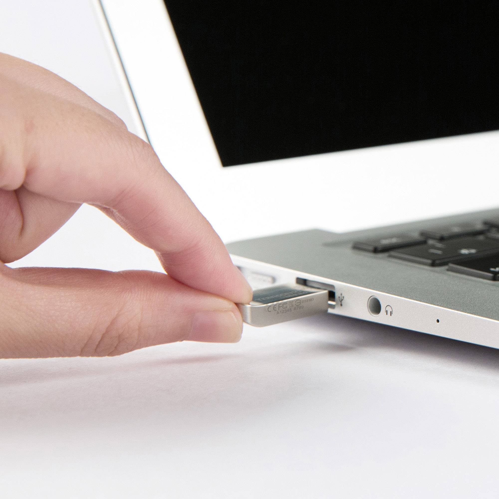 Hand steckt USB-Stick in Laptop. Fokus auf Technik. Umgebung nicht sichtbar. 