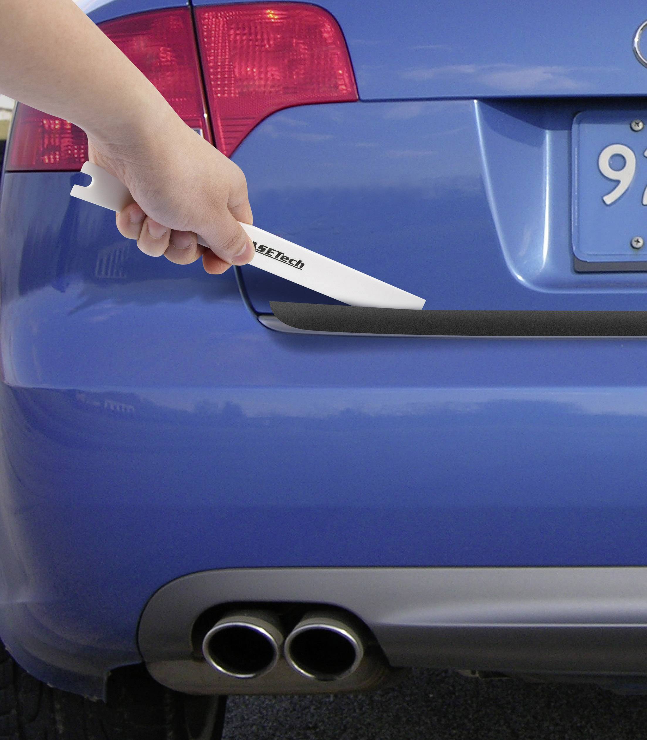 Eine Hand hält ein weißes Küchenmesser nahe der Rückseite eines blauen Autos, in der Nähe des Auspuffs.