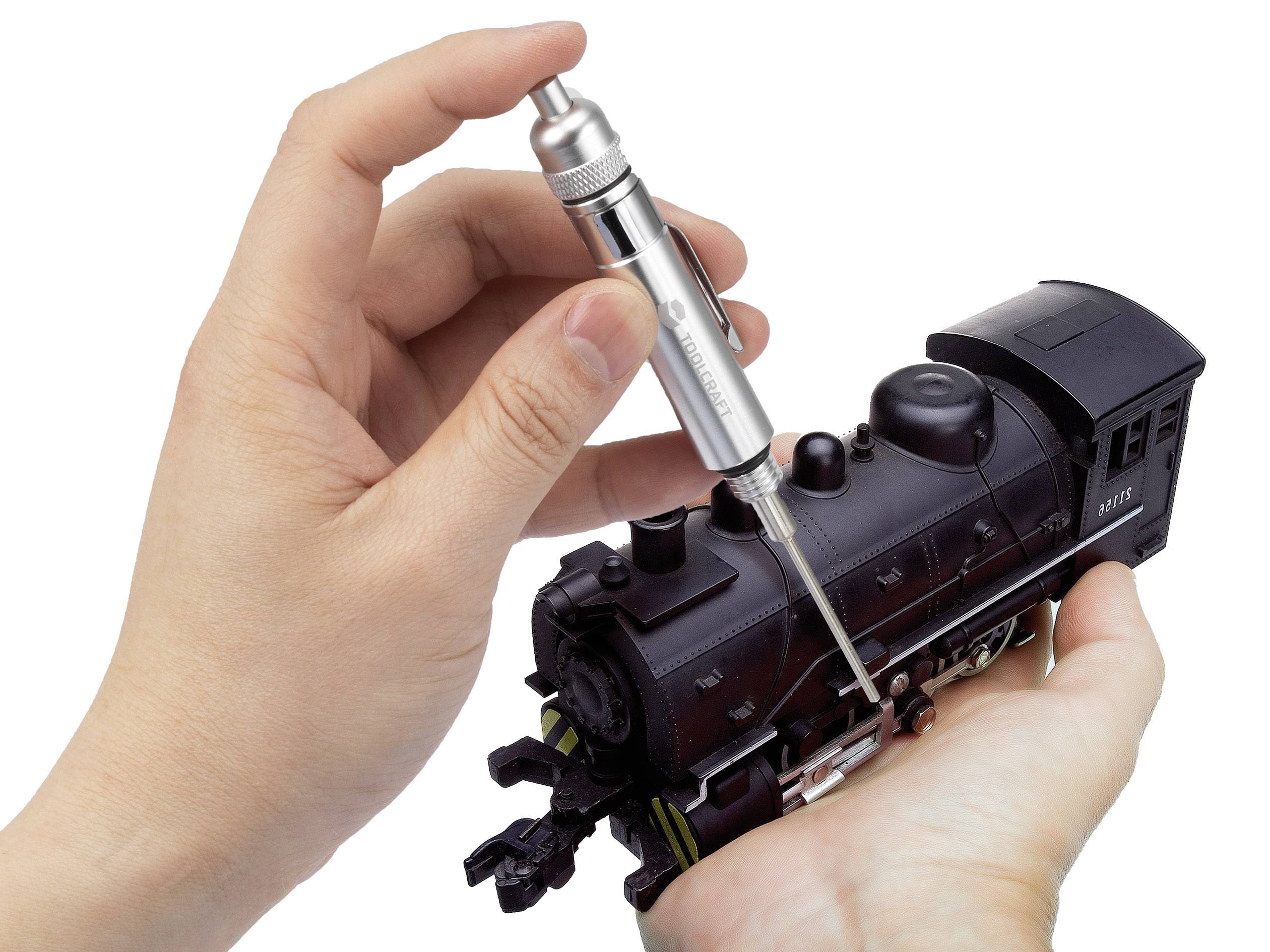 Eine Hand hält eine Miniaturlokomotive, während die andere mit einem Schraubendreher daran arbeitet.