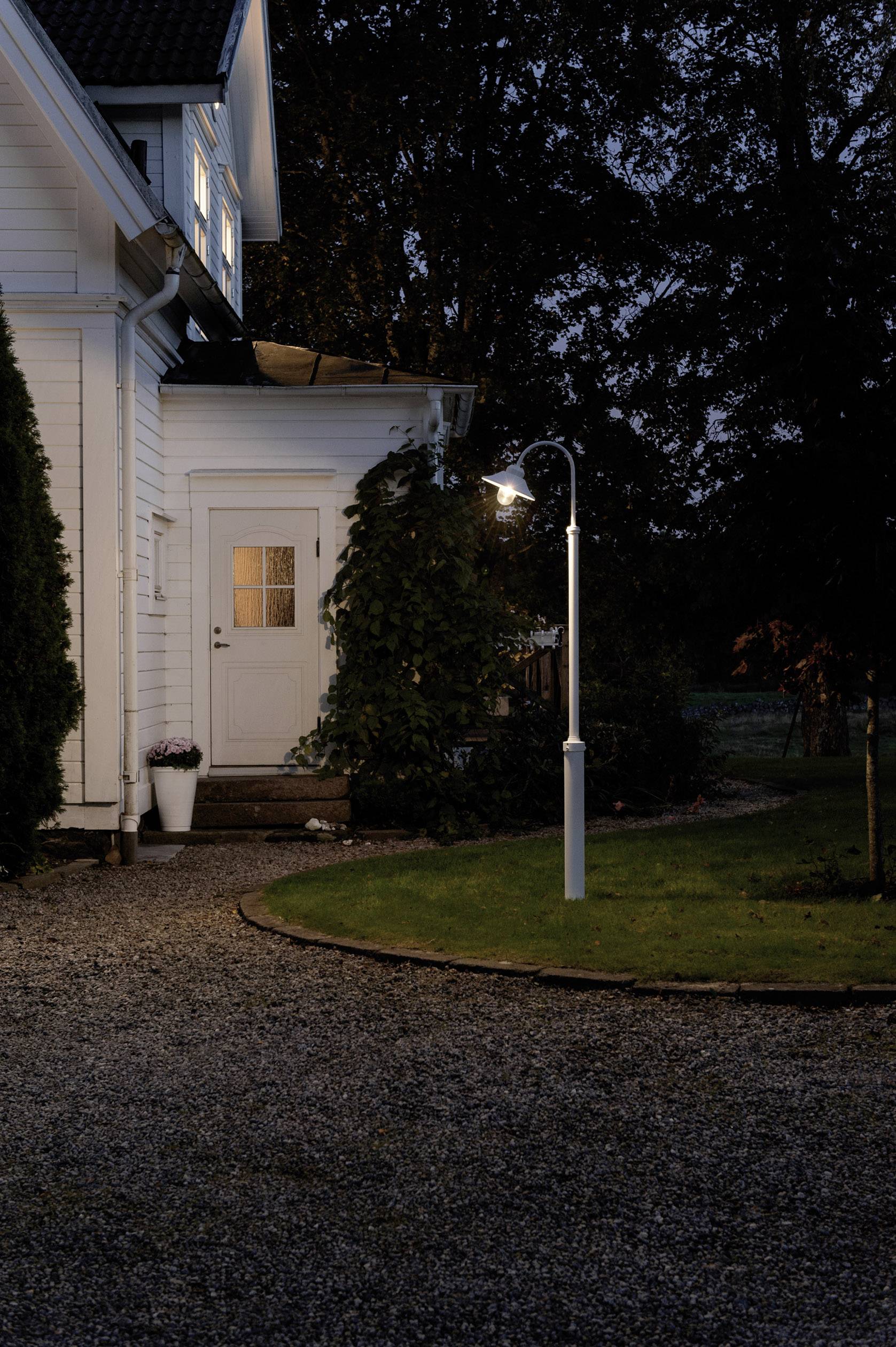 Ein beleuchteter Weglampenpfad führt zu einer weißen Haustür eines Hauses in der Dämmerung, umgeben von Grünpflanzen.