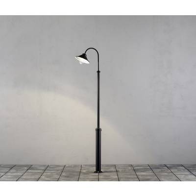 Eine einfache Laterne in einem minimalistischen Stil steht auf gepflastertem Boden vor einer grauen Wand.