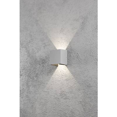 Wandleuchte mit quadratischem Gehäuse strahlt Licht nach oben und unten auf grob strukturierte, graue Wand. Minimalistisches Design.