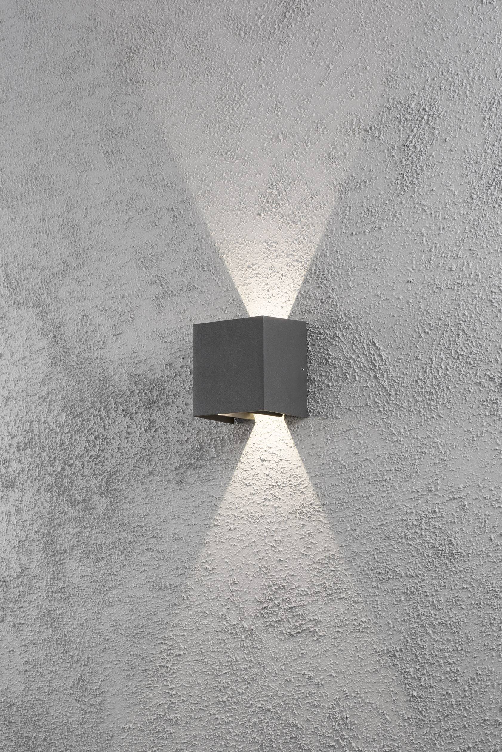 Eine graue Wandleuchte strahlt Licht nach oben und unten auf eine strukturierte Wandoberfläche.