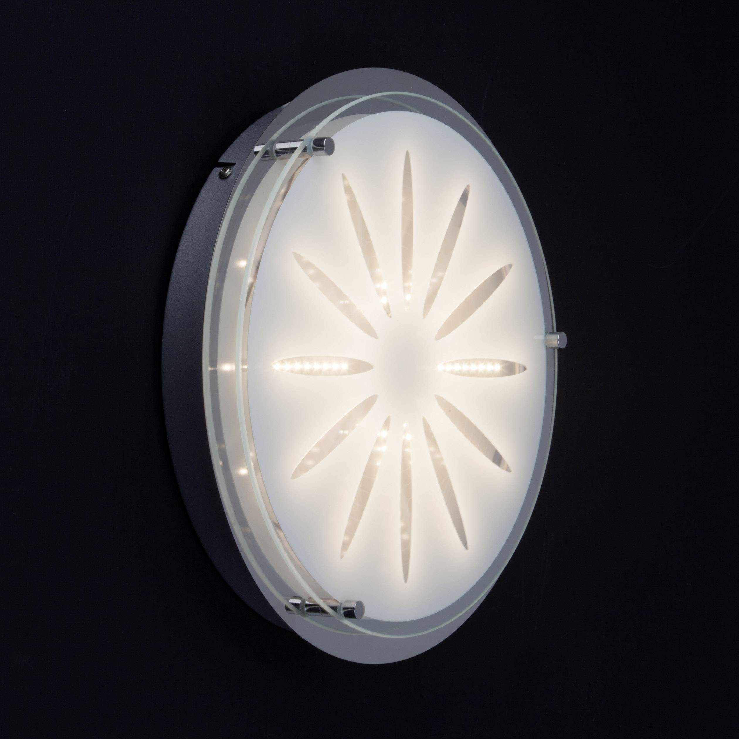Runde Wandlampe mit LED-Leuchten, strahlt sternförmiges Muster auf schwarzer Wand. Modernes, minimalistisches Design.