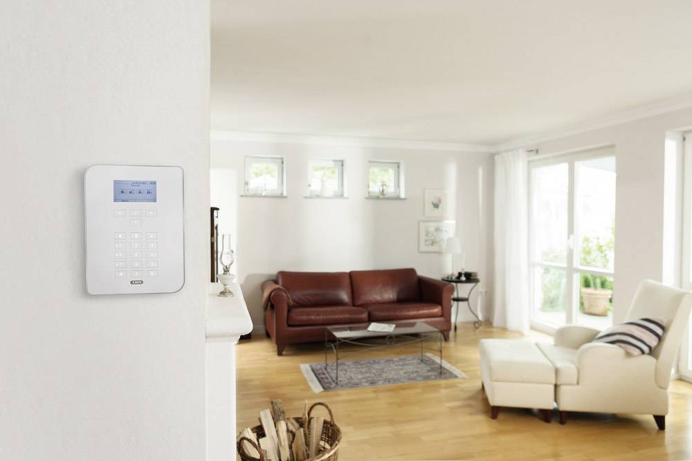 Ein Wohnzimmer mit Ledersofa, Sessel und Couchtisch. Ein digitales Bedienfeld ist an der Wand montiert. Helle, moderne Einrichtung.