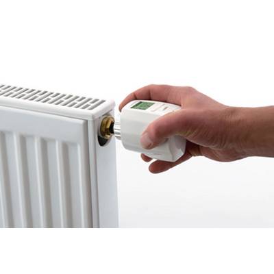 Eine Hand dreht den Thermostat eines weißen Heizkörpers.