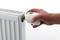 Eine Hand dreht den Thermostat eines weißen Heizkörpers.
