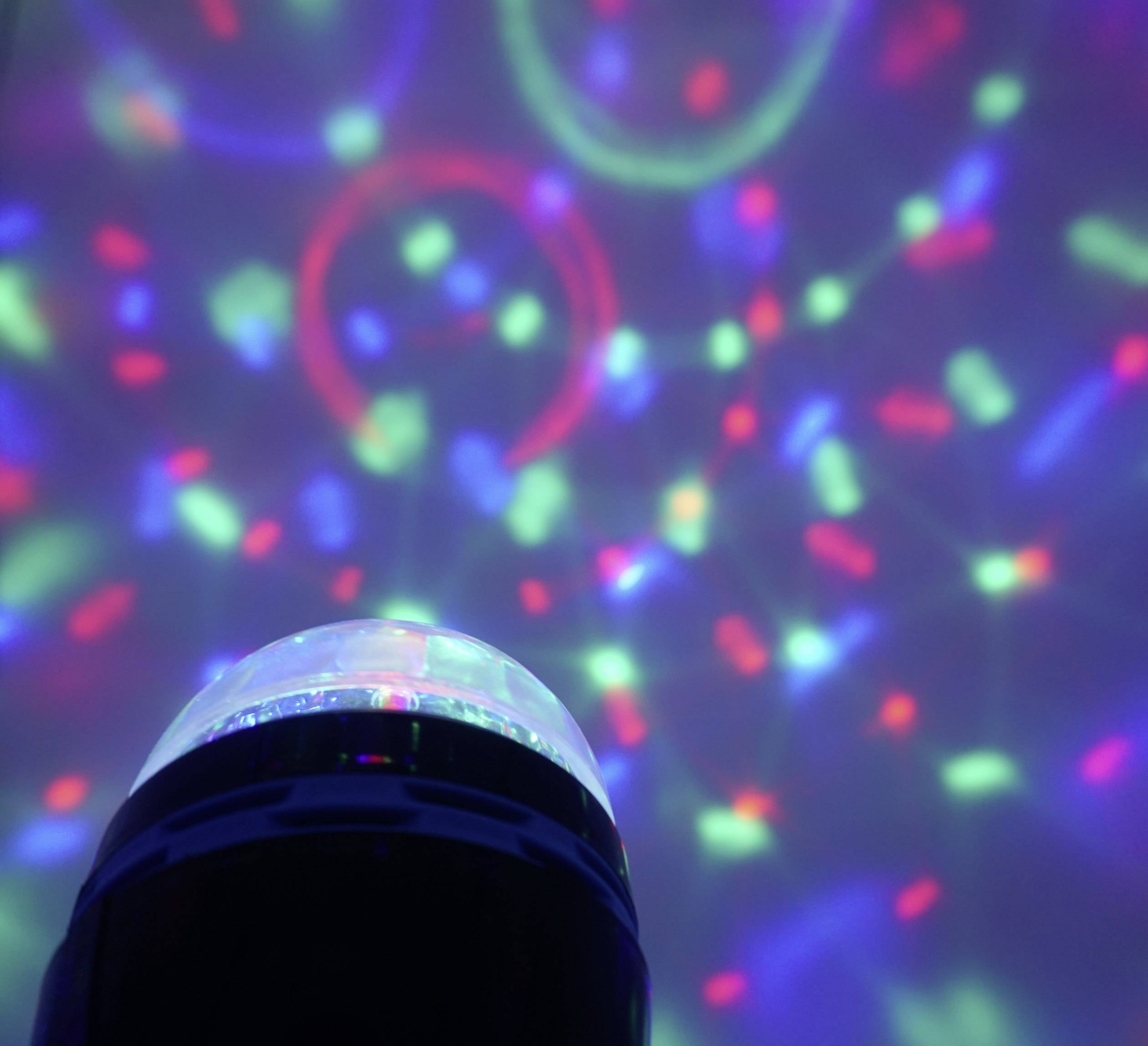 Eine schwarze Disco-Lampe projiziert bunte Lichtpunkte und Kreise in Rot, Grün und Blau auf eine weiße Wand.