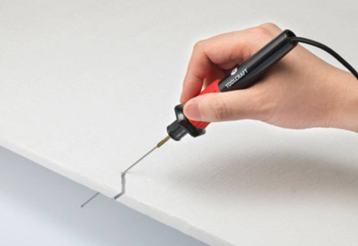 Eine Hand hält einen heißen Drahtschneider, schneidet präzise durch ein weißes Material, vermutlich Schaumstoff oder Kunststoff.