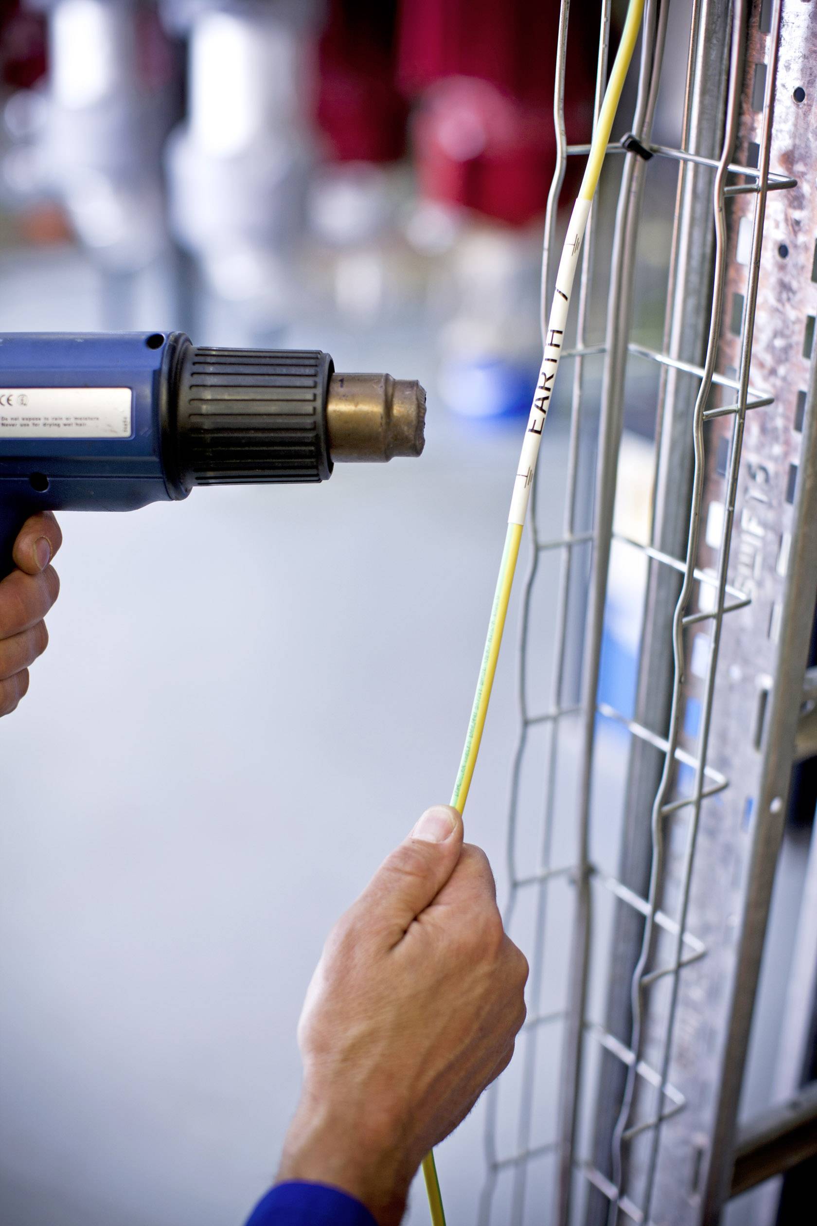 Eine Person schrumpft mit einem Heißluftgebläse ein beschriftetes Kabel am Metallgitter für Kabelmanagement zusammen.