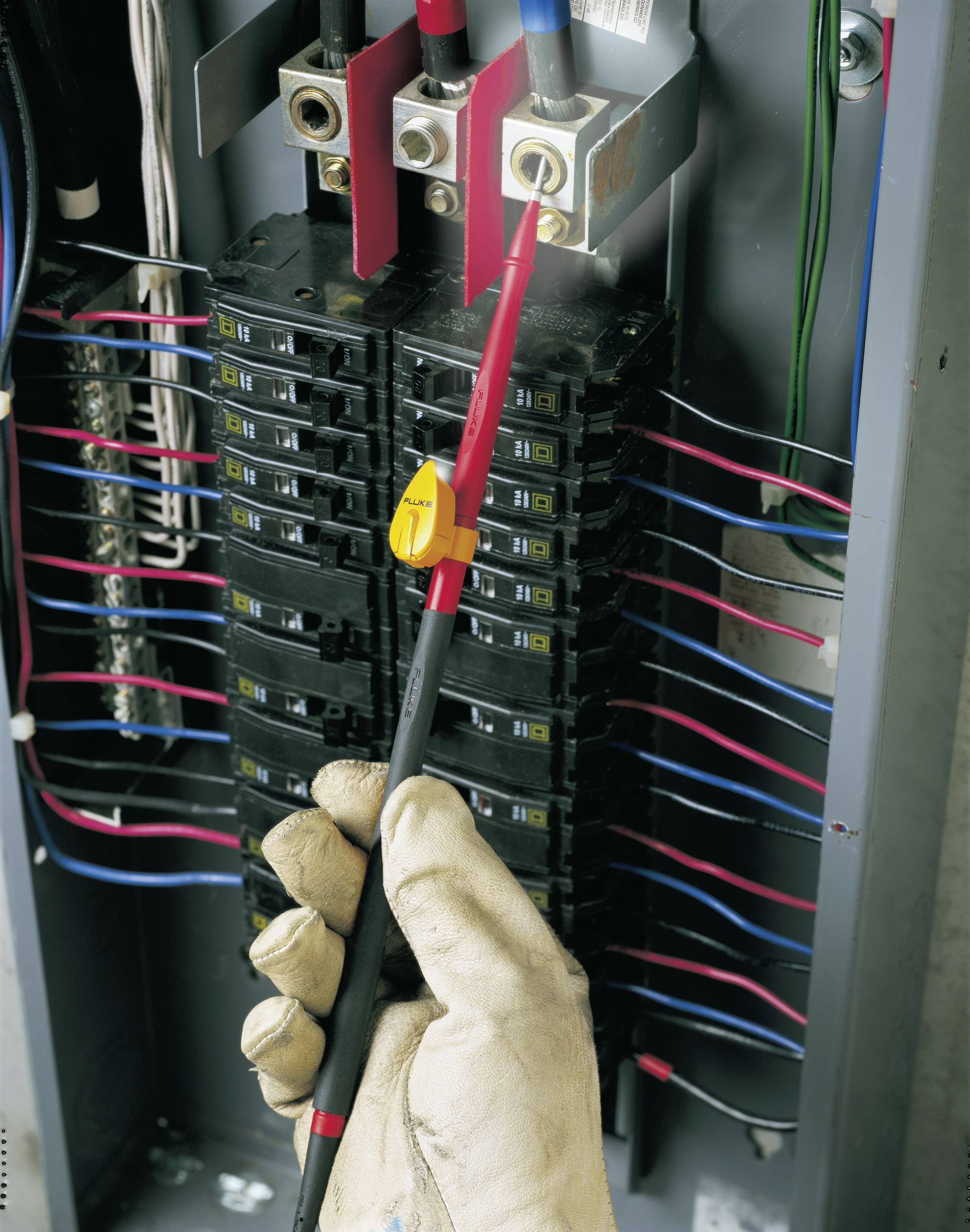 Ein Elektrikerhandschuh hält einen Spannungsprüfer an einem Sicherungskasten voller Kabel, um die Spannung zu prüfen.