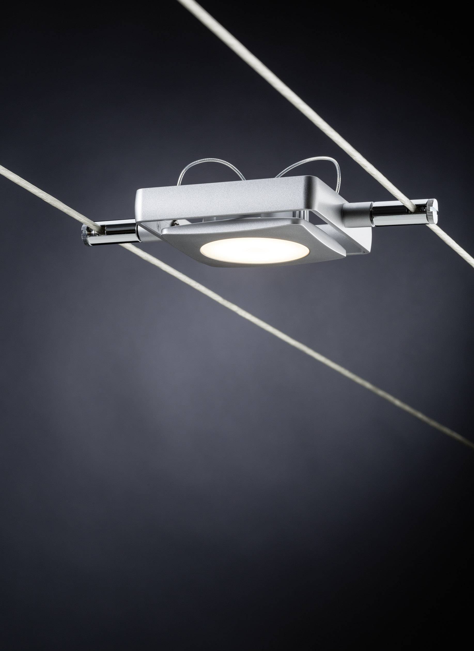 Ein modernes Deckenlicht mit rechteckigem Design und LED-Lampe, aufgehängt zwischen zwei dünnen Drähten vor dunklem Hintergrund.