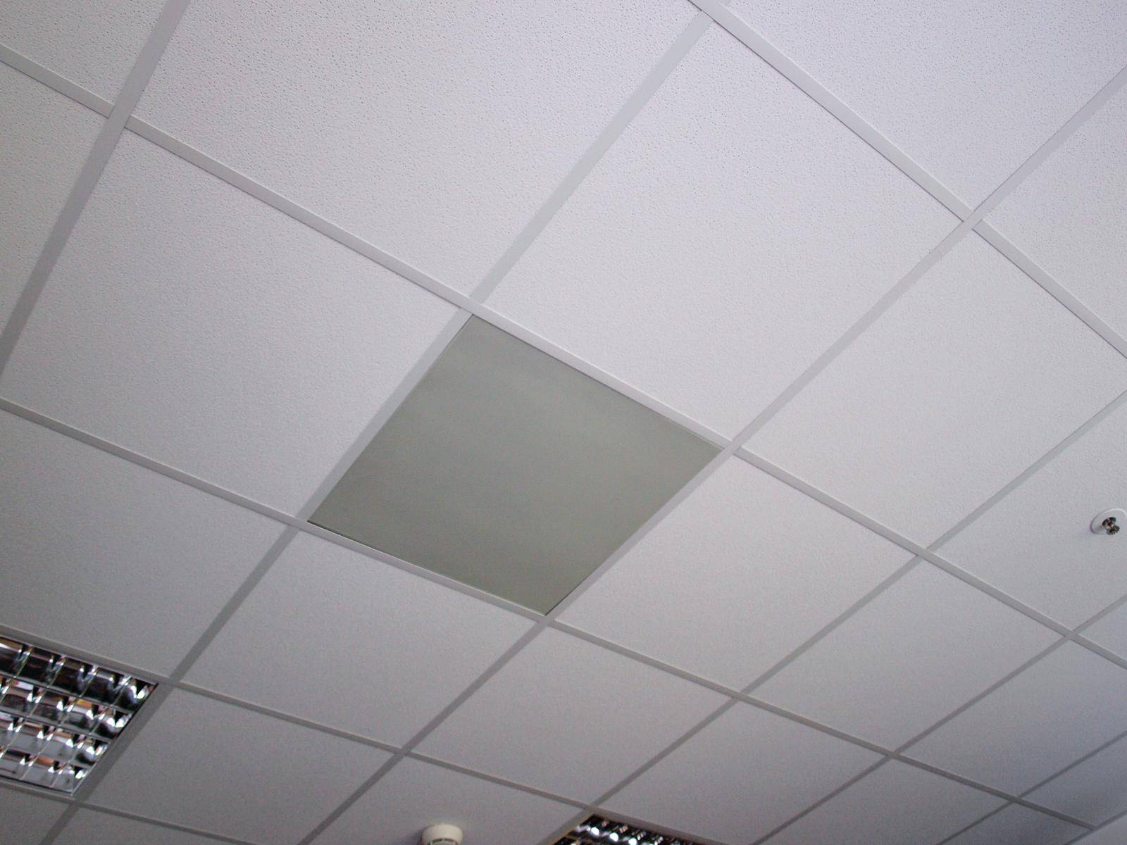 Weiße Decke mit Rasterdeckenplatten. Eine matte graue Platte bildet einen Kontrast in der Mitte. Einige Lichter sind sichtbar.