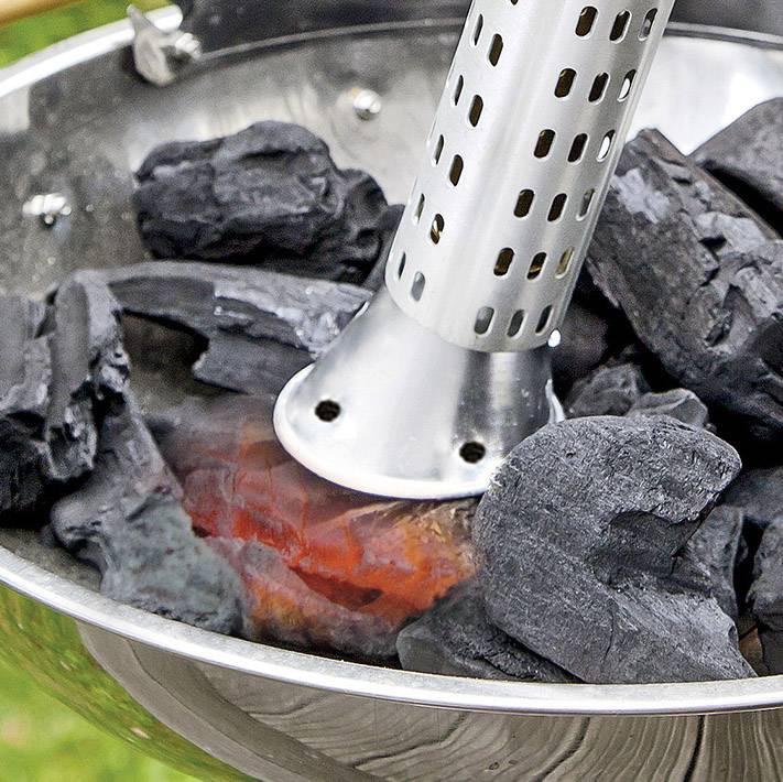 Ein elektrischer Grillanzünder erhitzt Holzkohle in einer Metallschale. Die Kohle beginnt zu glühen und es entstehen heiße, rote Stellen.