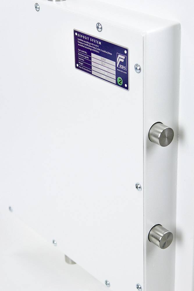 Ein weißes, rechteckiges Gerät mit Metallelementen und einem blauen Etikett mit technischen Spezifikationen an einer Wand montiert.