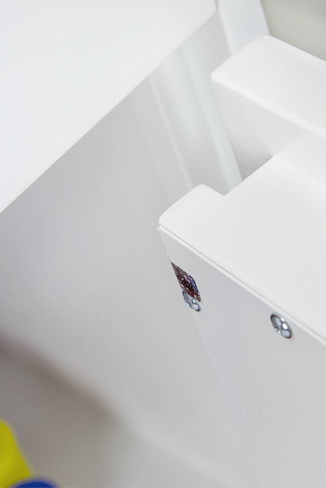 Nahaufnahme eines weißen Möbelstücks mit Schrauben und einer kleinen bunten Markierung an der Ecke.