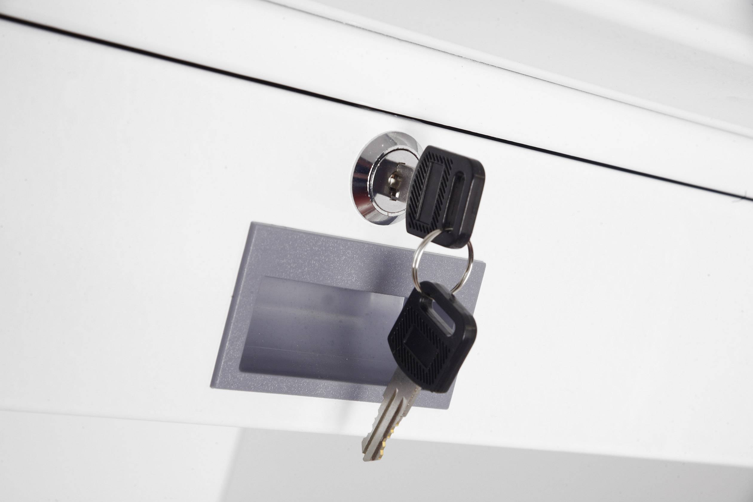 Ein Schlüsselsatz steckt in einem weißen Schloss an einer Schublade. Zwei schwarze Schlüssel hängen am Schlüsselbund.