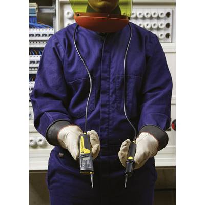 Elektriker in Schutzkleidung hält Spannungsprüfer vor Schaltschrank.