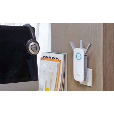 Ein WLAN-Extender ist an eine Steckdose angeschlossen. Neben einem aufgeklappten Laptop und einem Headset auf einem Tisch platziert.