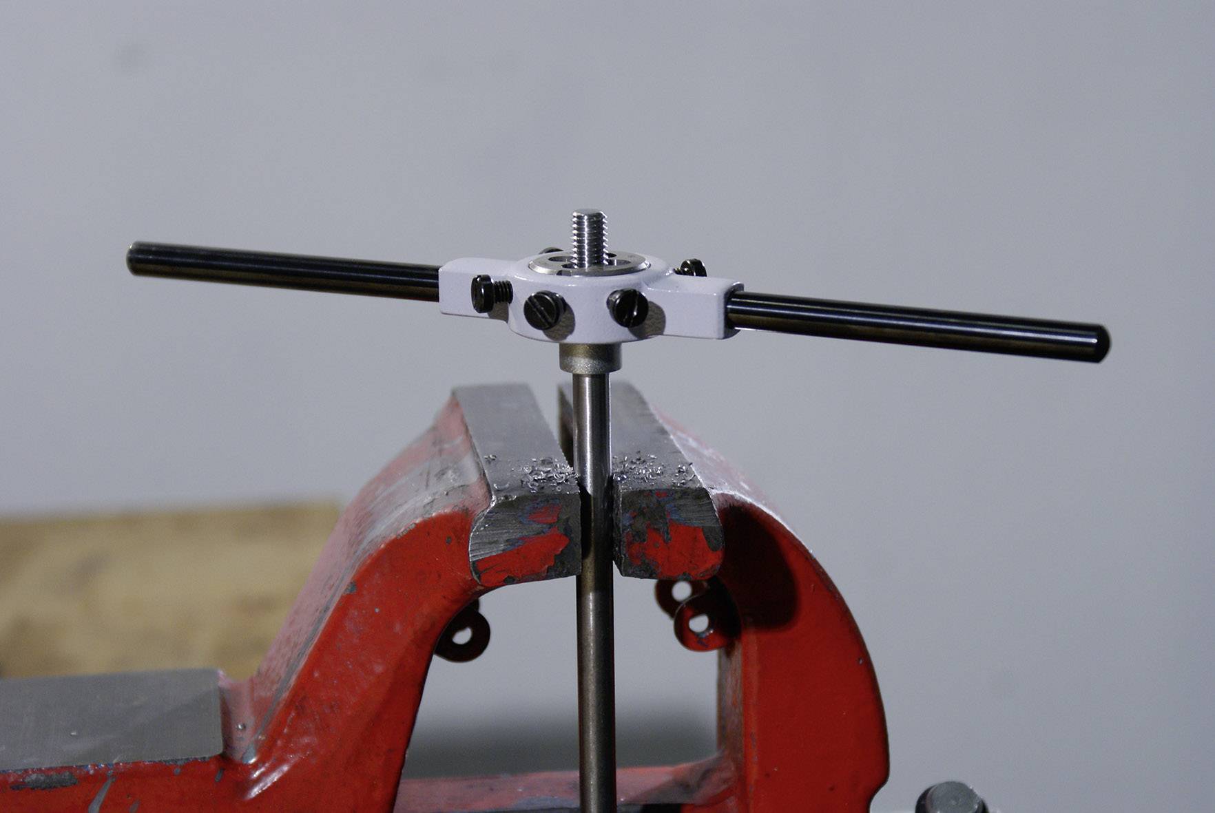 Ein Metallstab wird mit einem Schraubstock fixiert. Oben befindet sich ein Gewindebohrer, der ein Gewinde schneidet.