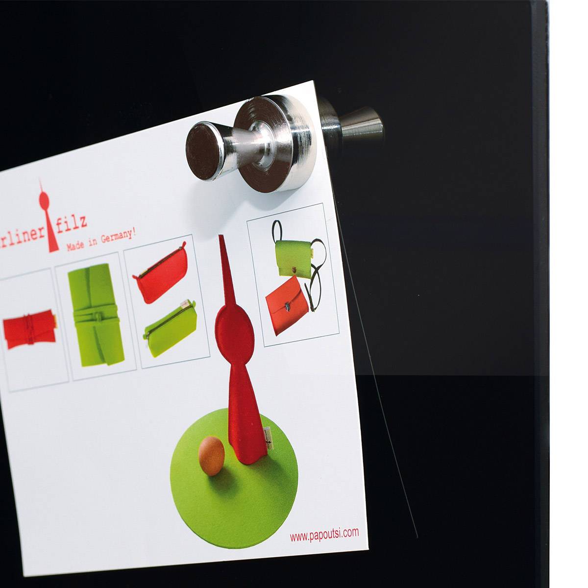 Eine rote Magnet-Küchenuhr mit einem weißen Zettel daran, zeigt eine Produktbeschreibung mit roten und grünen Filzbeuteln.