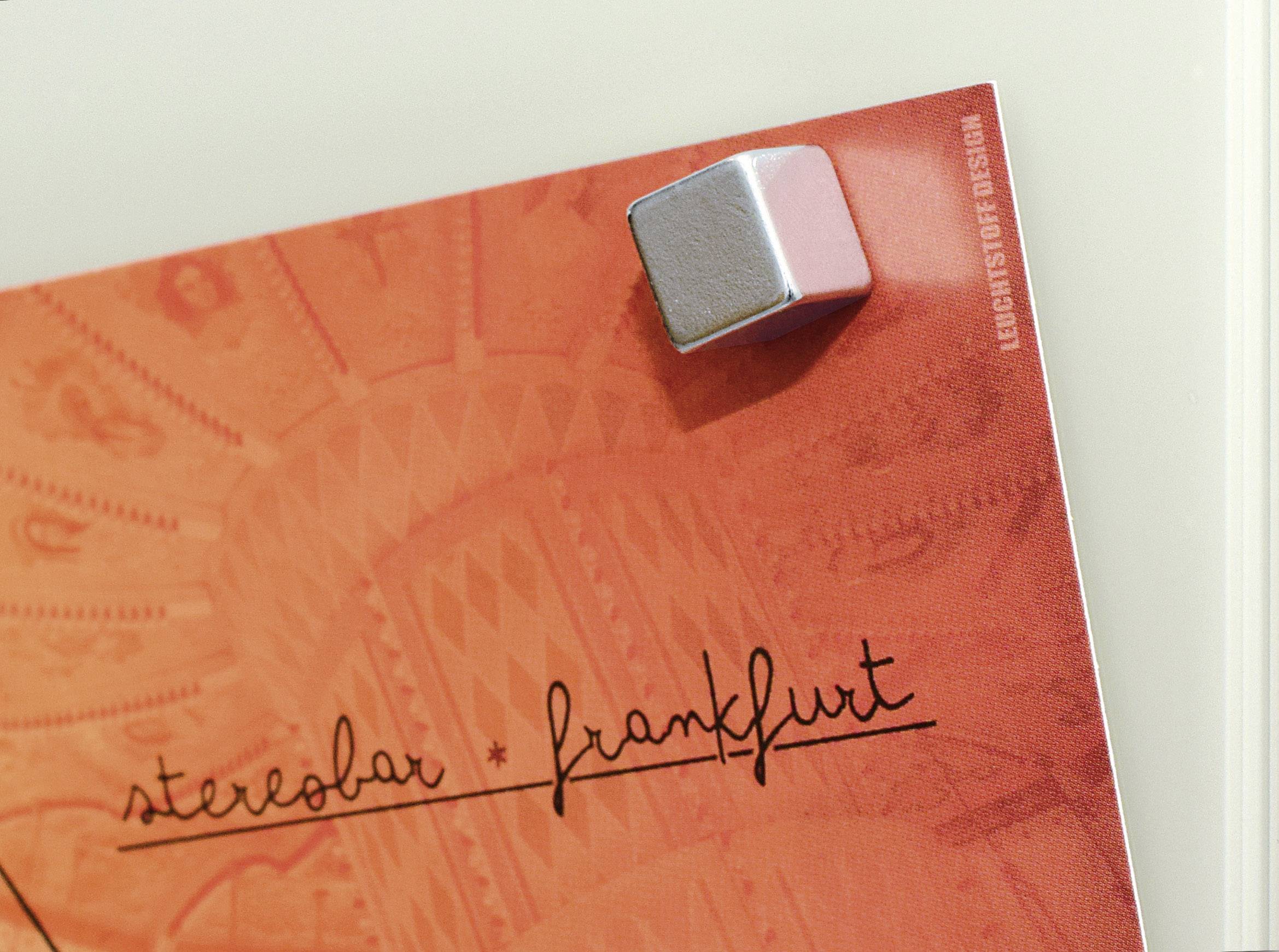 Ein rot-oranges Poster mit der Aufschrift 'stereobar frankfurt' steckt unter einem silbernen Magneten an einer Oberfläche.