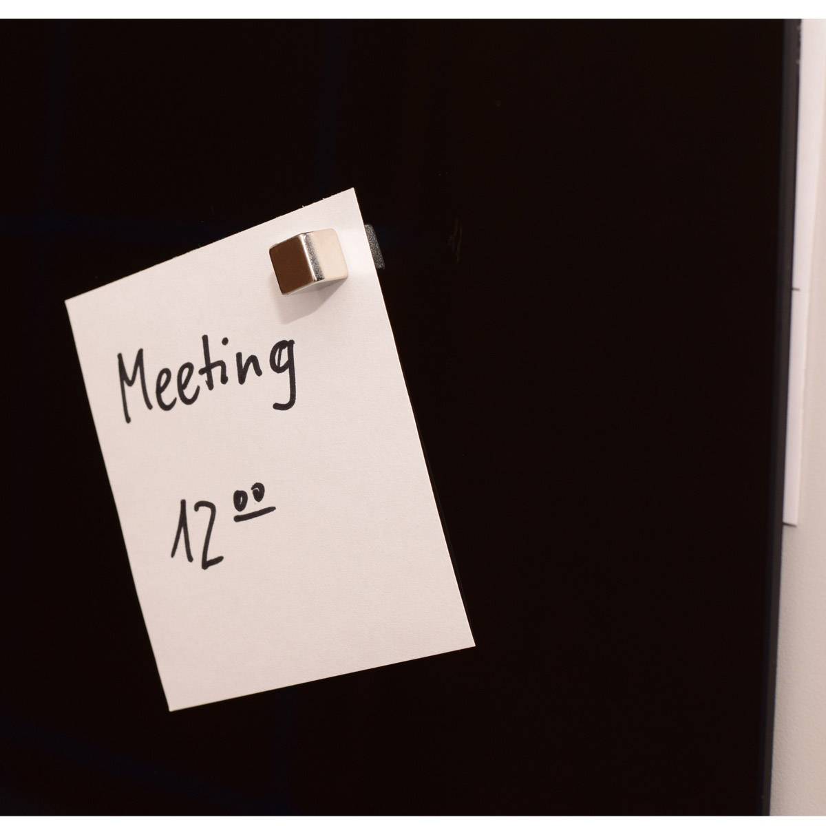 Ein Notizzettel mit der Aufschrift 'Meeting 12:00' hängt an einer schwarzen Tafel.