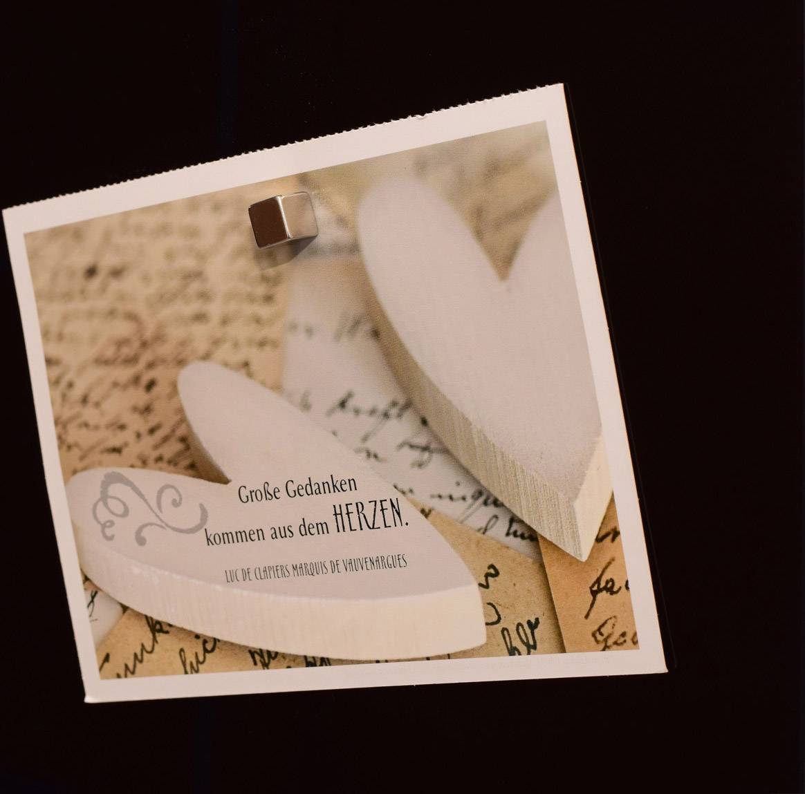 Ein Zettel mit der Aufschrift 'Große Gedanken kommen aus dem HERZEN' liegt auf einem Vintage-Hintergrund mit zwei Holzherzen.